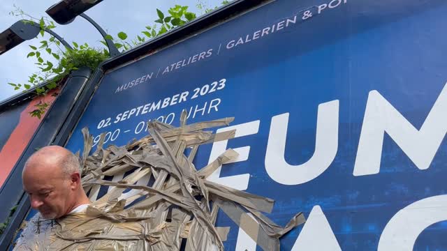 Kulturkleber klebt sich aus Protest an Plakatwand